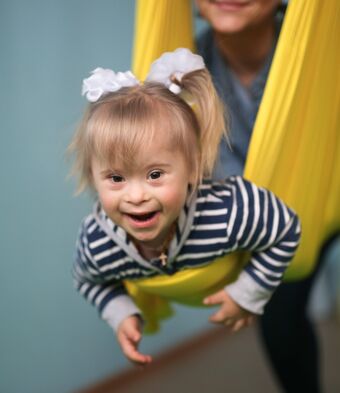 Little girl with Down syndrome held in a yellow sling