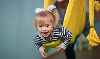 Little girl with Down syndrome held in a yellow sling