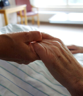 Carer hands holding frail palliative care care home nursing
